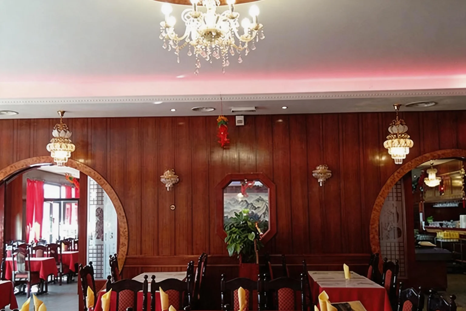 La salle : murs en bois rouge, lustres, tables aux nappes rouges